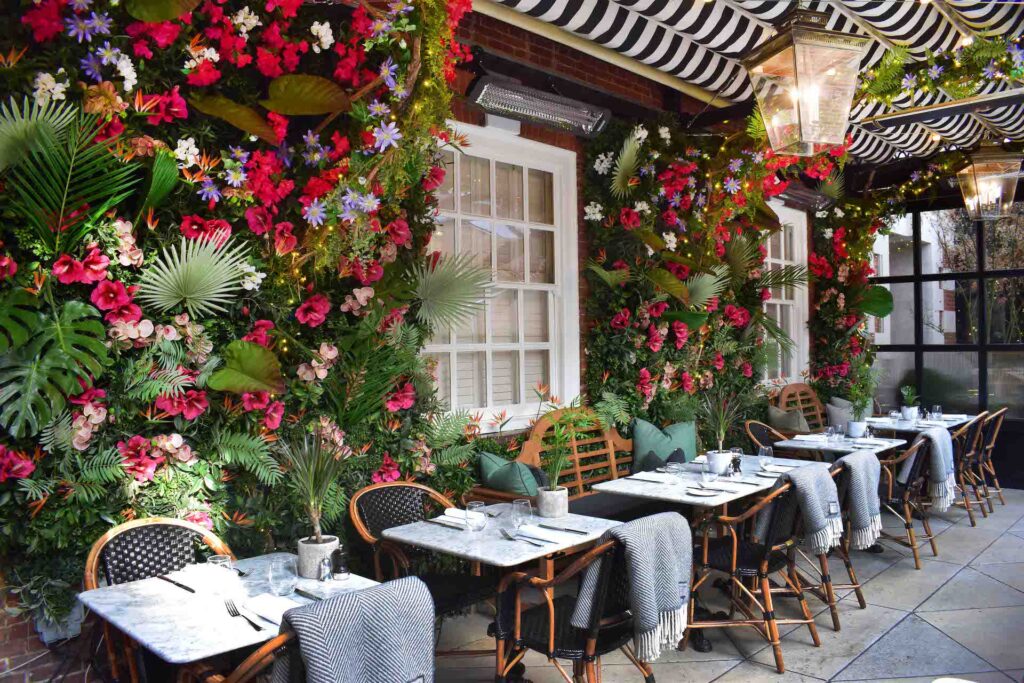 Schattig openluchtrestaurant met gebloemde muren en dekens over rieten stoelen om de klanten warm te houden, samen met een Bromic-verwarming